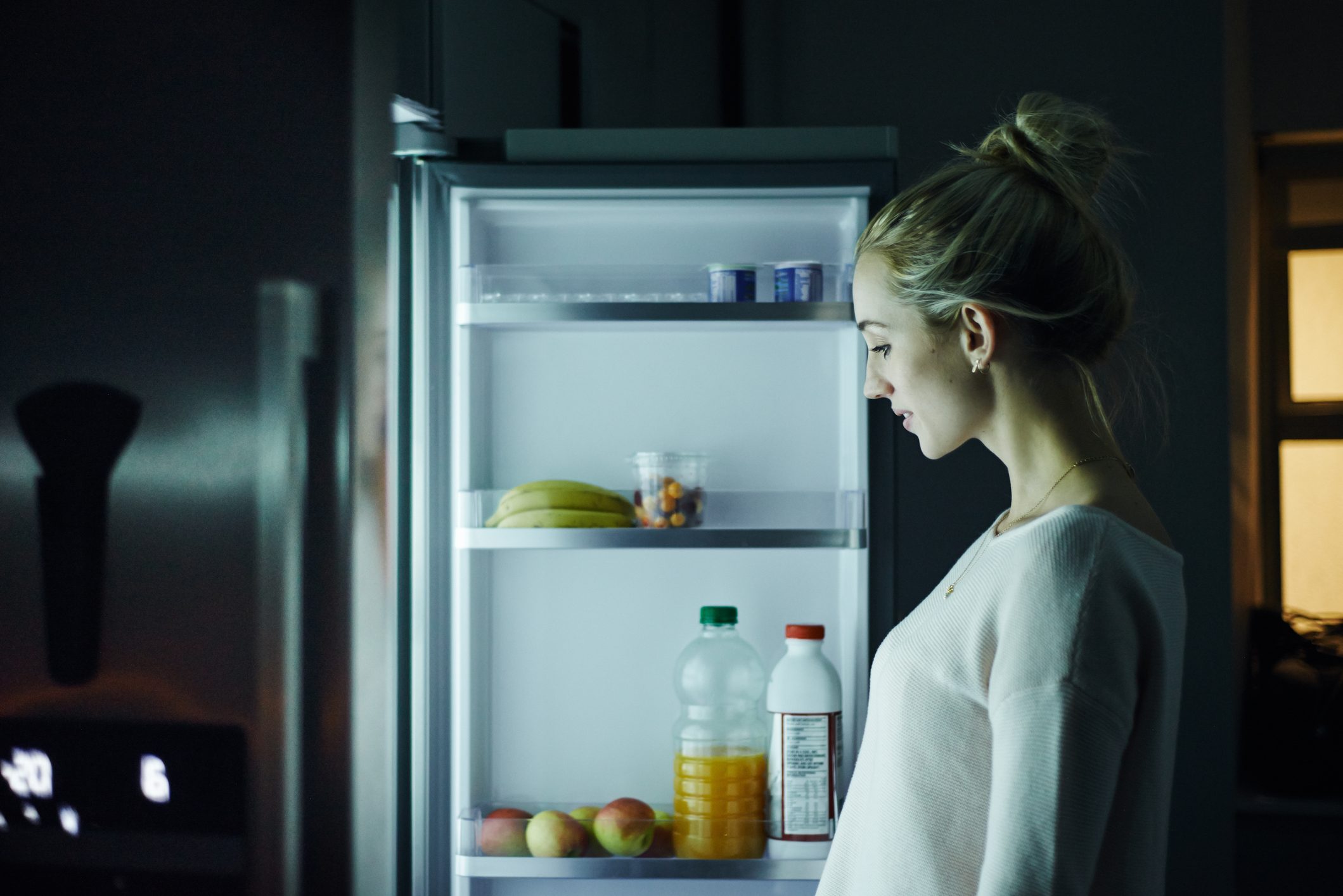 Shot of a young woman opening the fridge at night in her home
