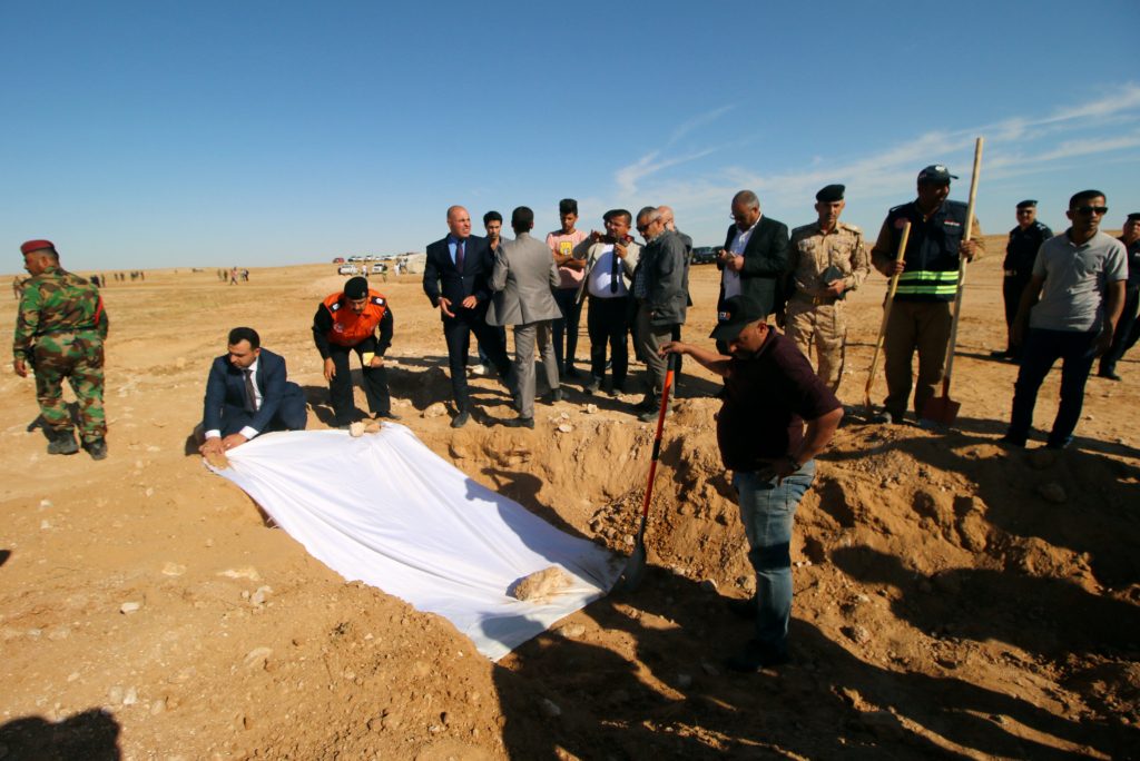 أعضاء من الدفاع المدني العراقي ومسؤولون يغطون عظام ضحايا المقبرة المكتشفة
